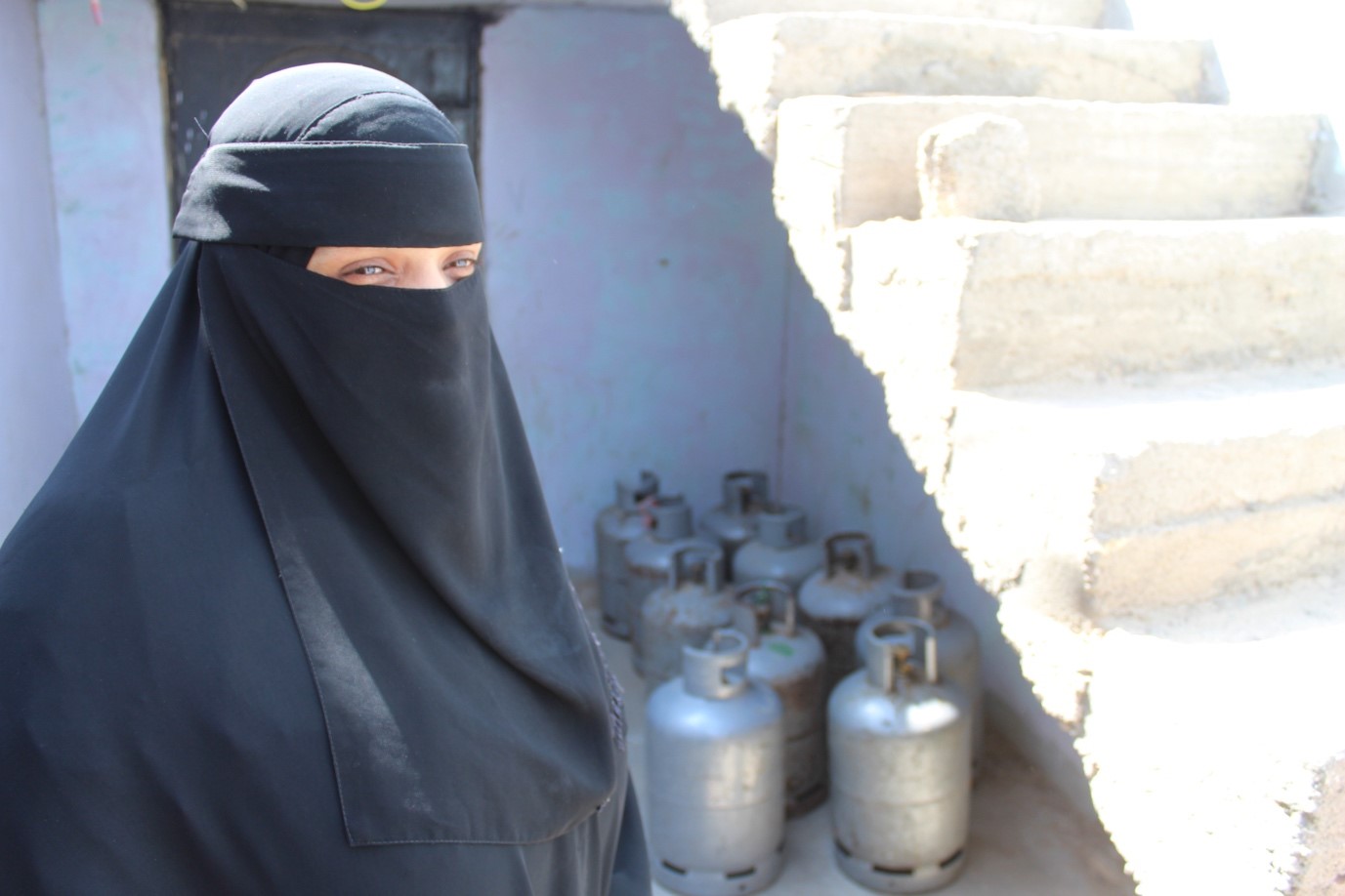 A woman in a black veil standing in front of gas cylinders.