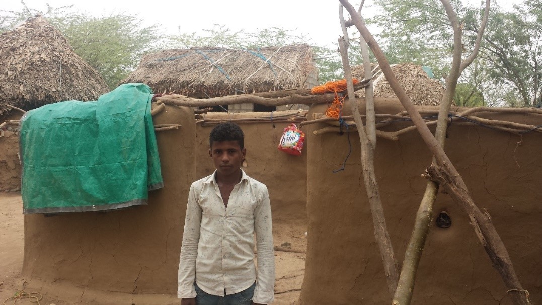 A boy standing in front of a mud house