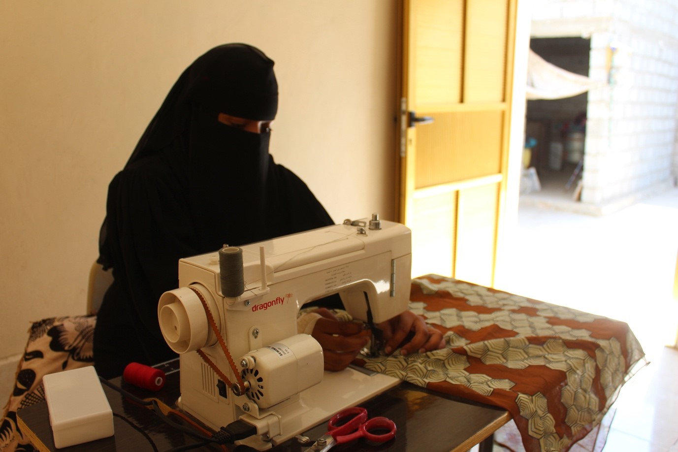 A woman wearing a black head covering using a sewing machine