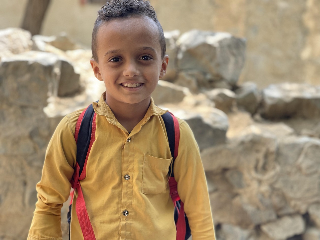 A young boy smiling and wearing a backpack