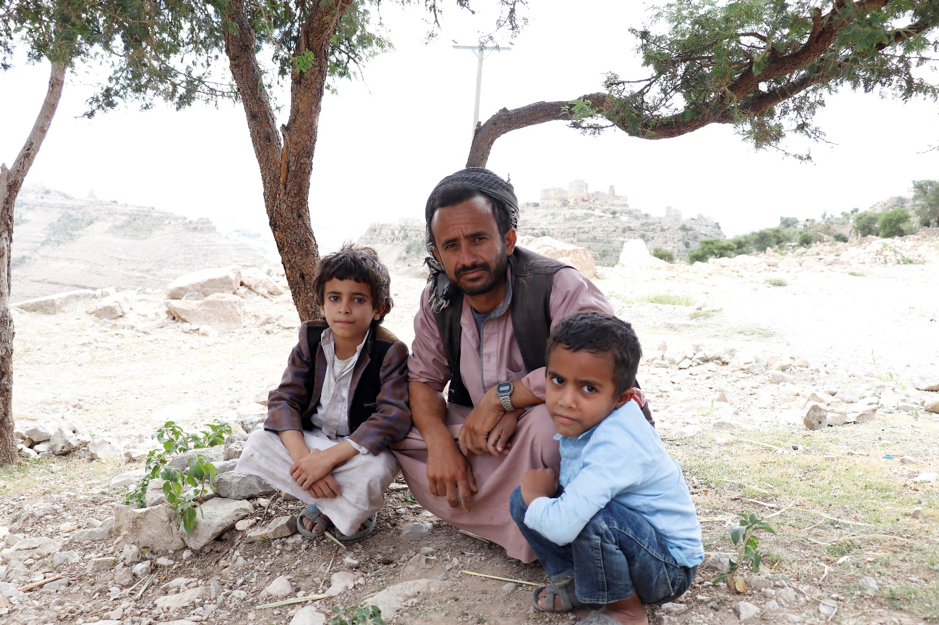 A man and two boys sitting under a tree