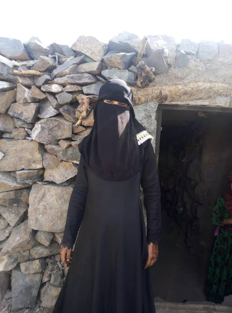 A woman wearing a black burqa standing in front of stone wall