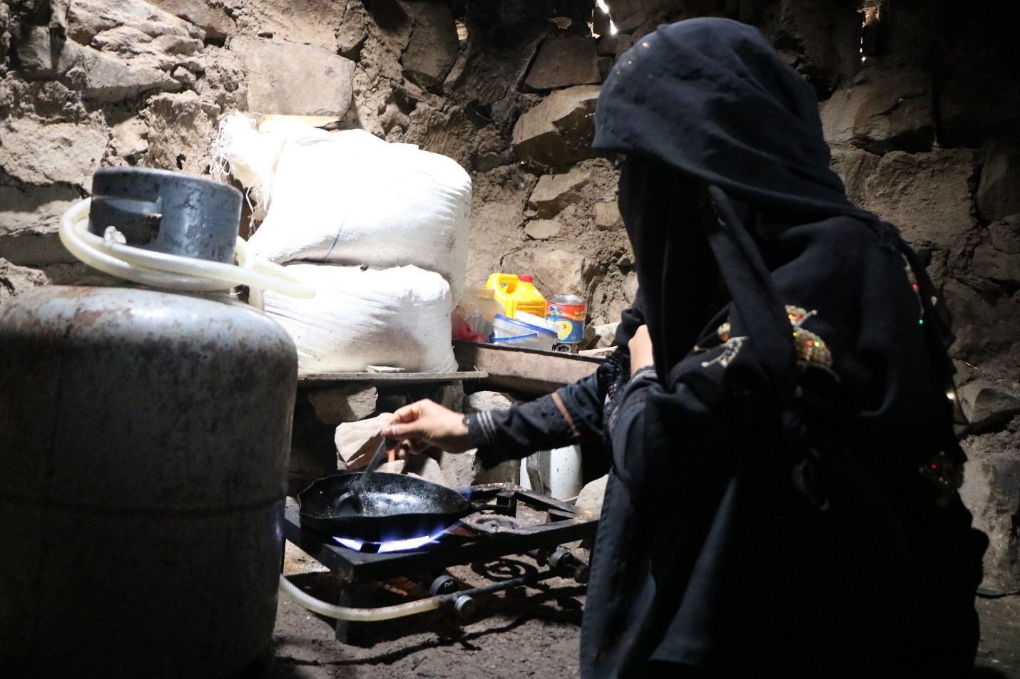 A woman wearing a black Burqa and cooking in a small kitchen