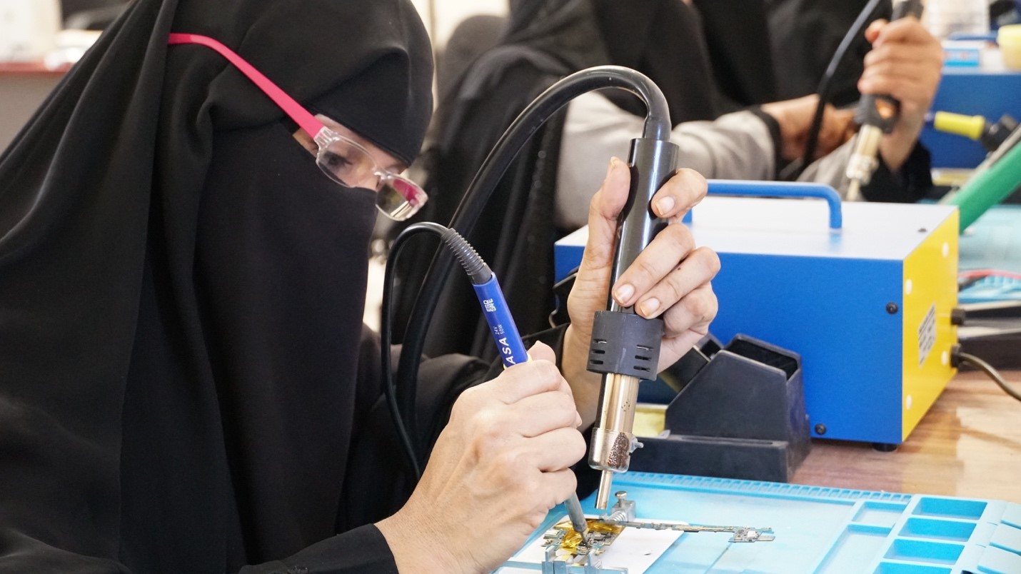 A woman wearing a black burqa working on a machine