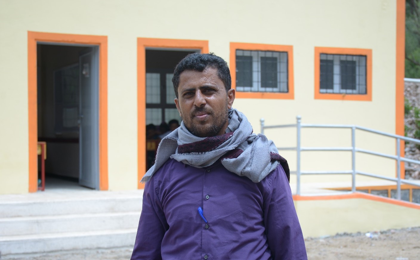 A man in purple shirt and grey scarf standing outside of a building