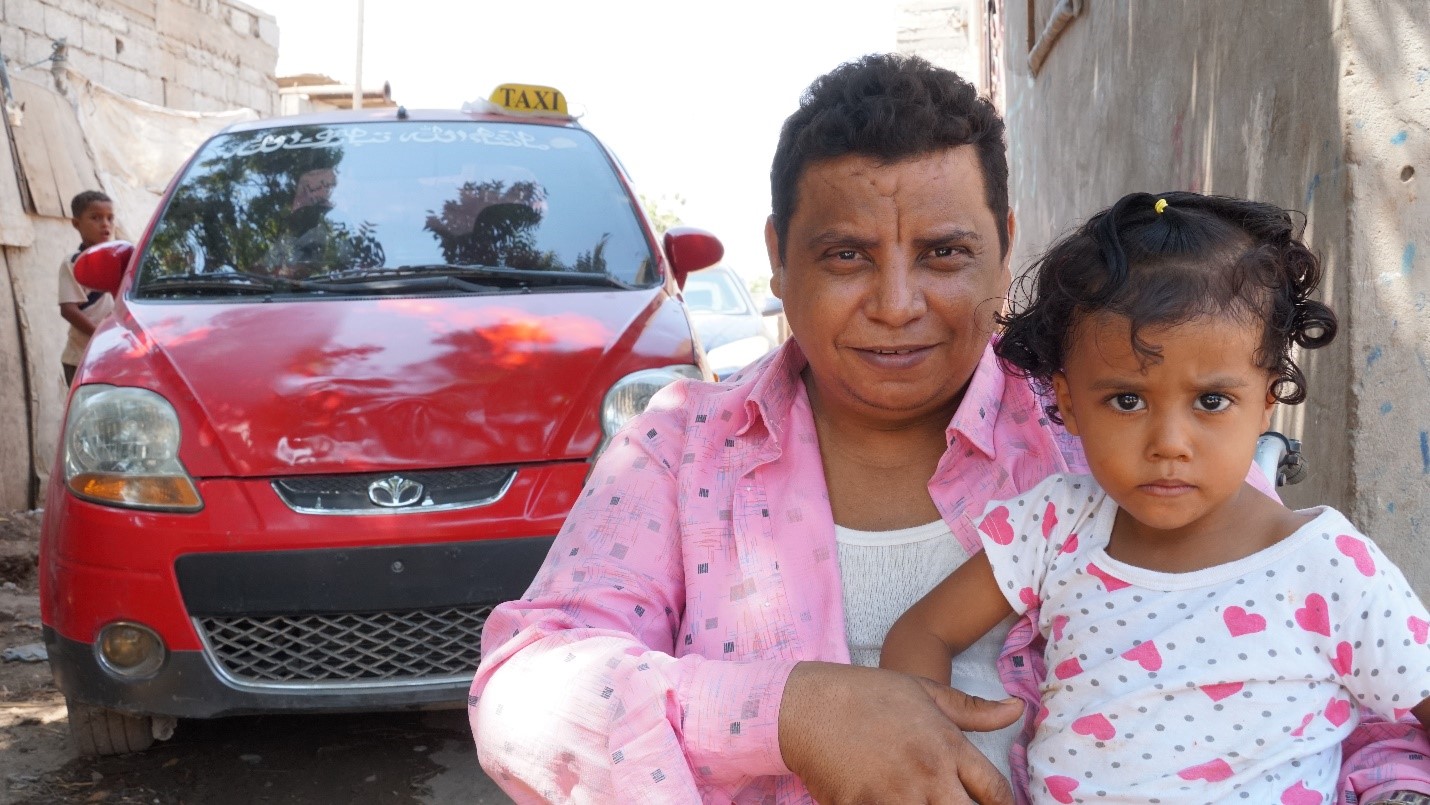 A person sitting holding a baby with a red car packed on the side