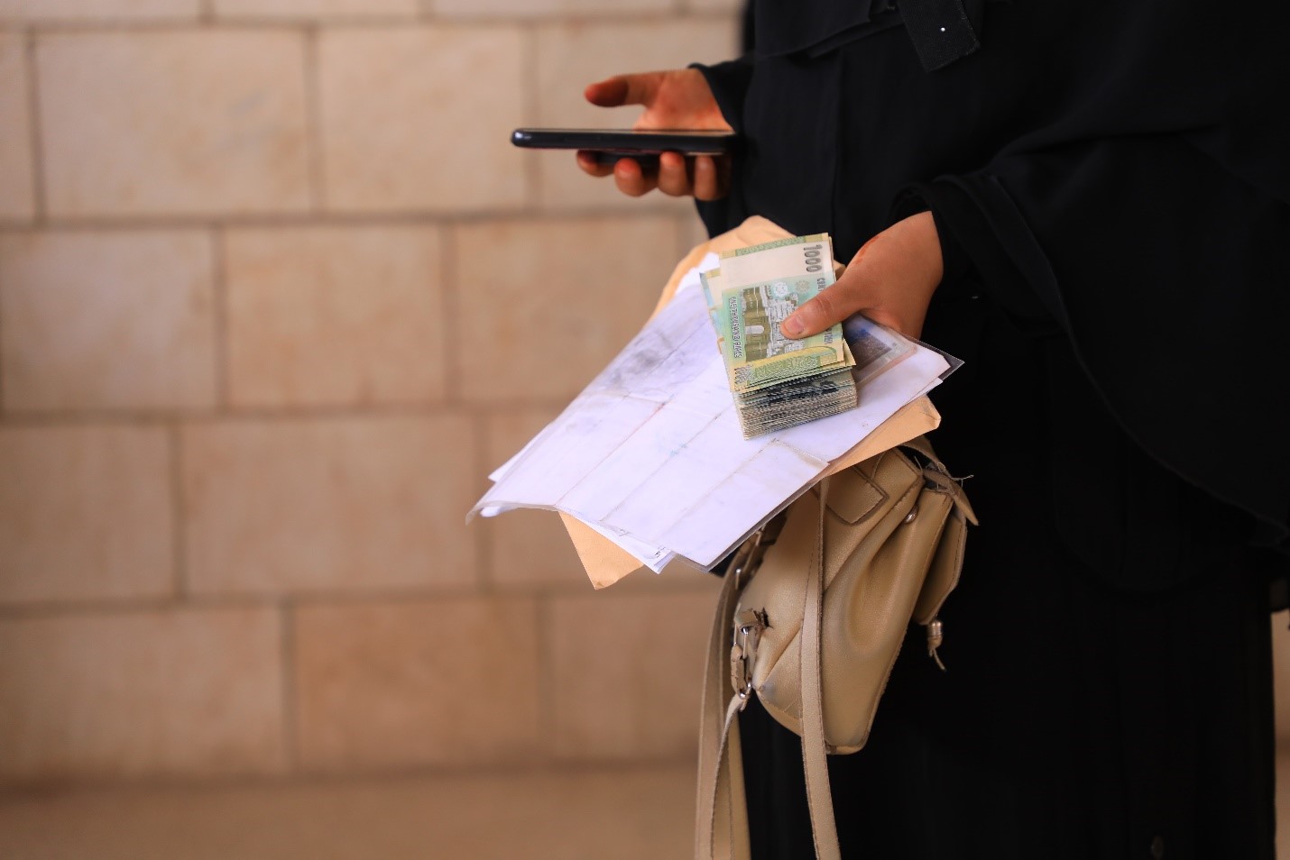 A woman in a black abaya holding a mobile phone and a money