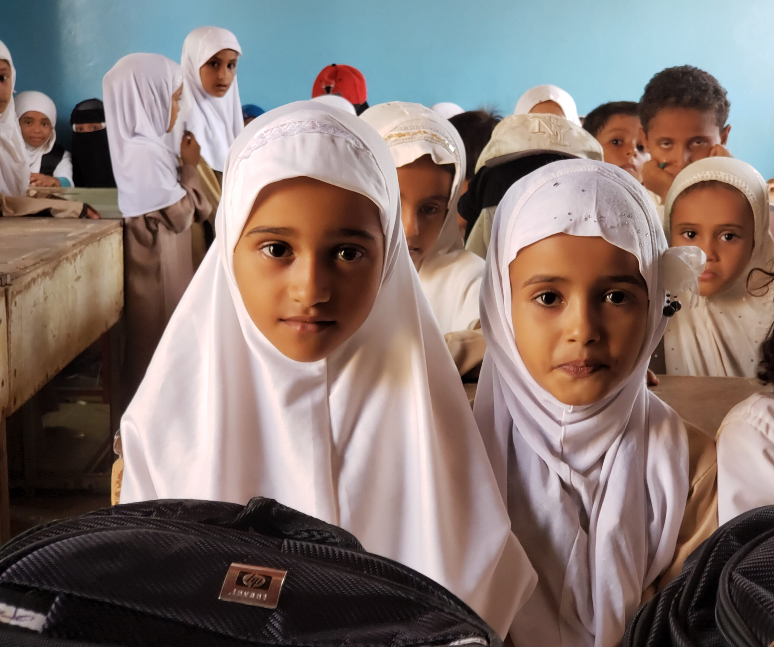 Two beatiful girls with wearing white headscarves sitting in class with other kids