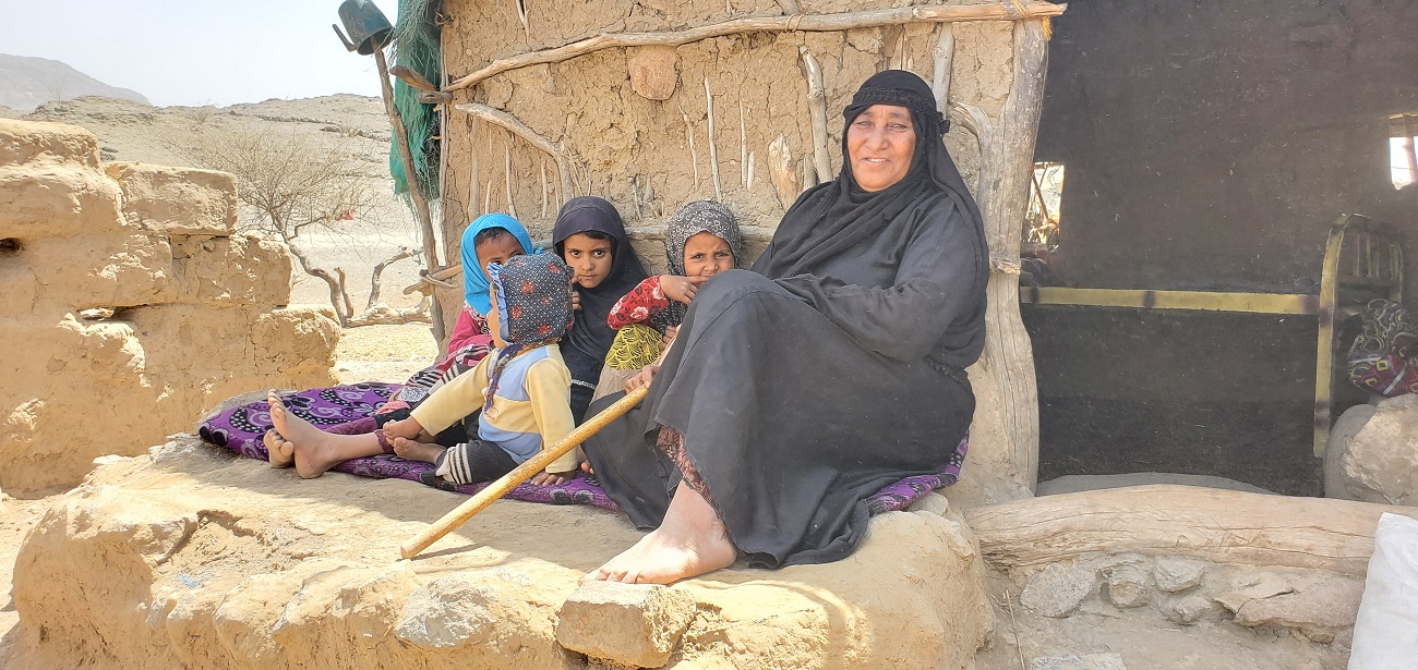 A woman and 3 kids sitting outside a mud house