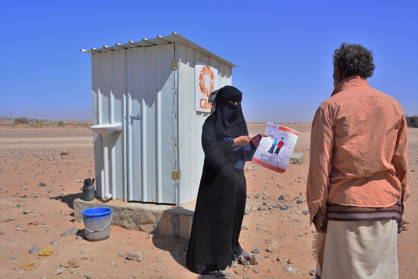 A woman in a burka holding a paper in front of a portable toilet.