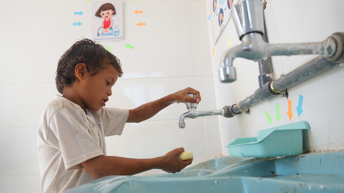 A small boy holding a soap on a running tap water