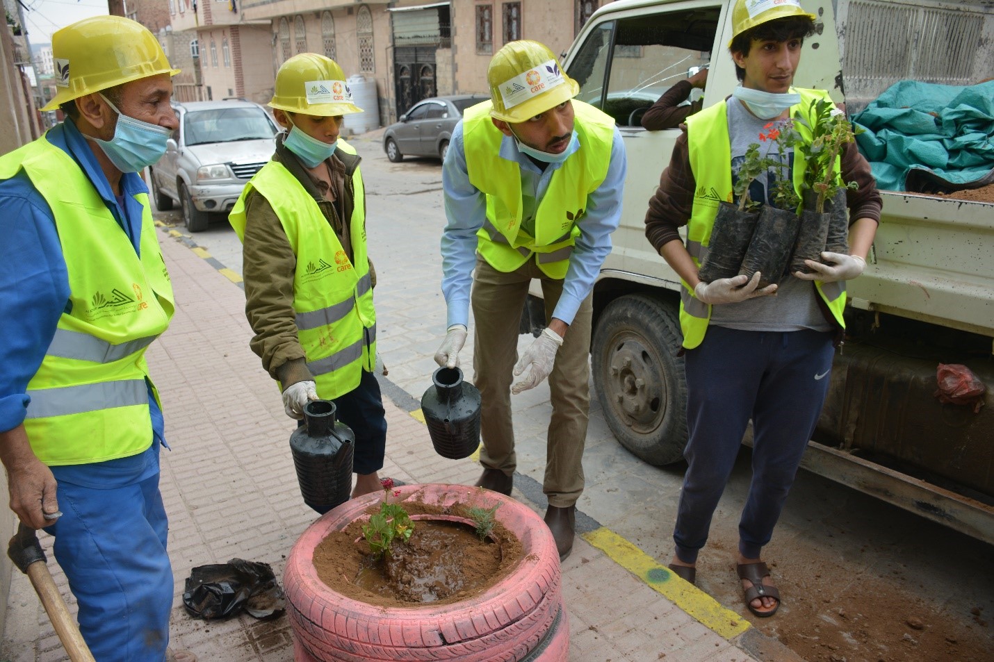 A group of men wearing safety vests and hats holding plants and water cans
