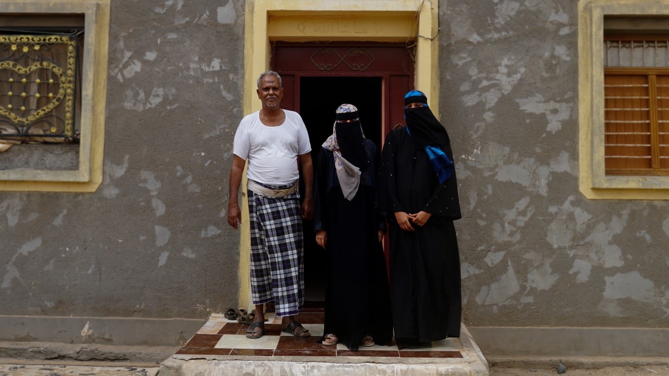 A man and two women standing in front of a house