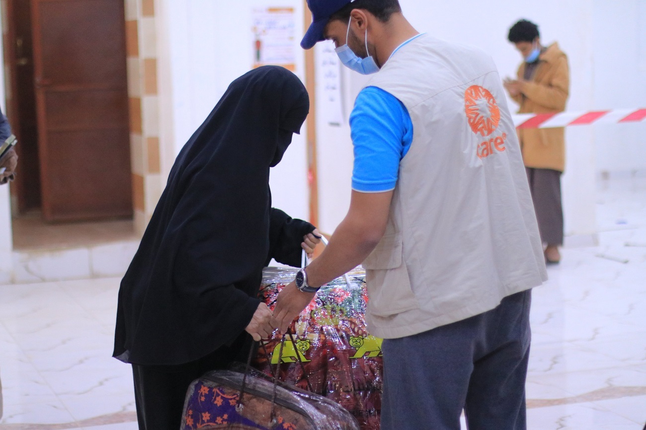 A man wearing a mask and a woman wearing a black head covering holding bags in their hands
