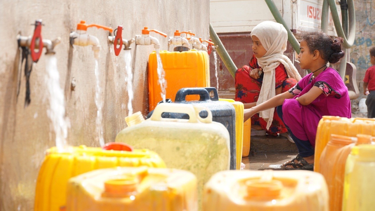 Two young girls fetching water form a tap with Jerrycans