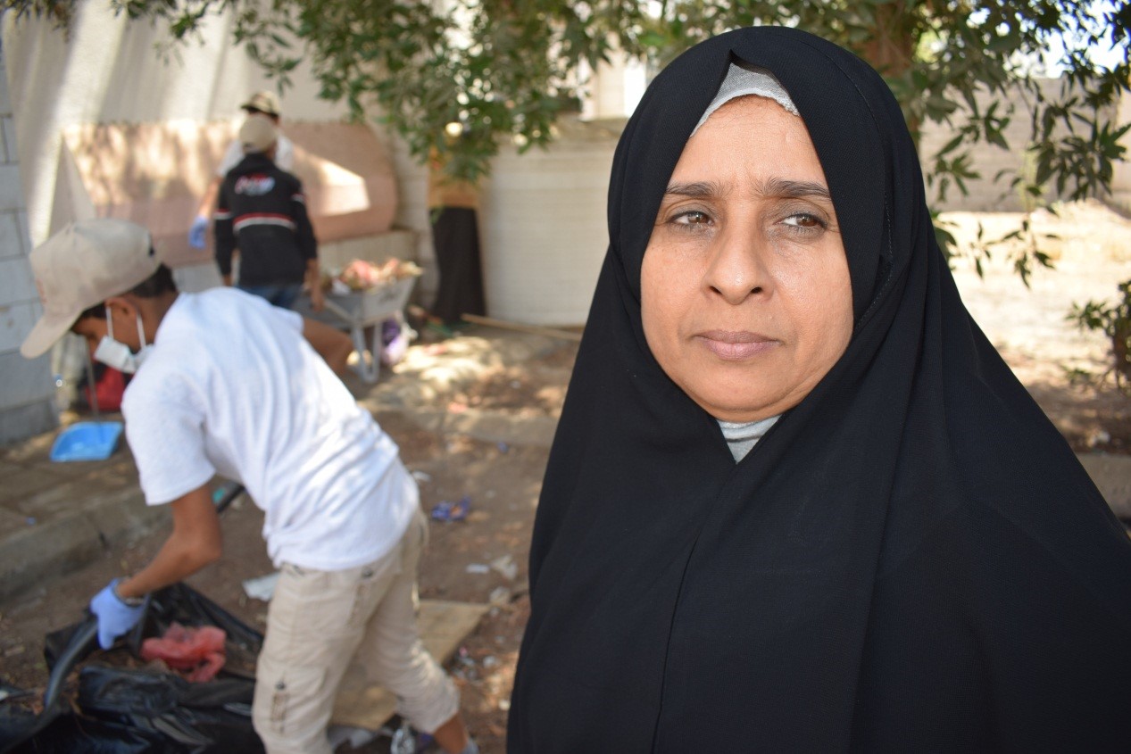 A woman wearing a black headscarf standing beside a garbage bin.