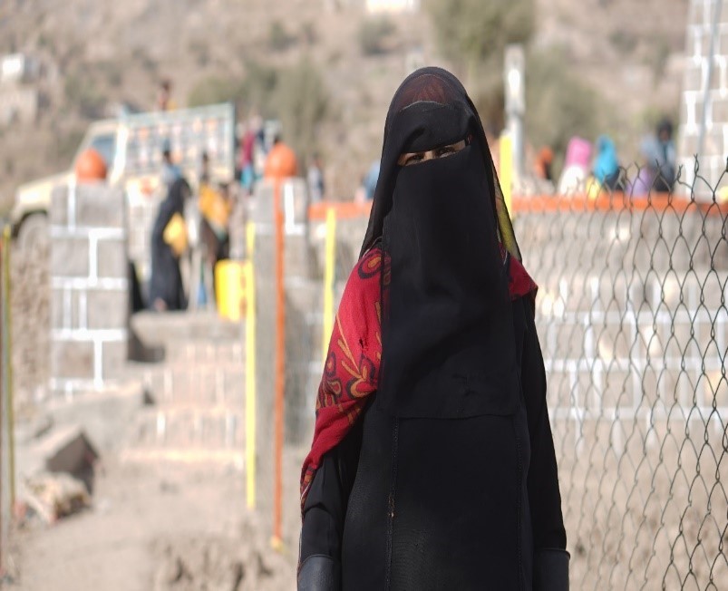Woman in black veil standing in front of fence,