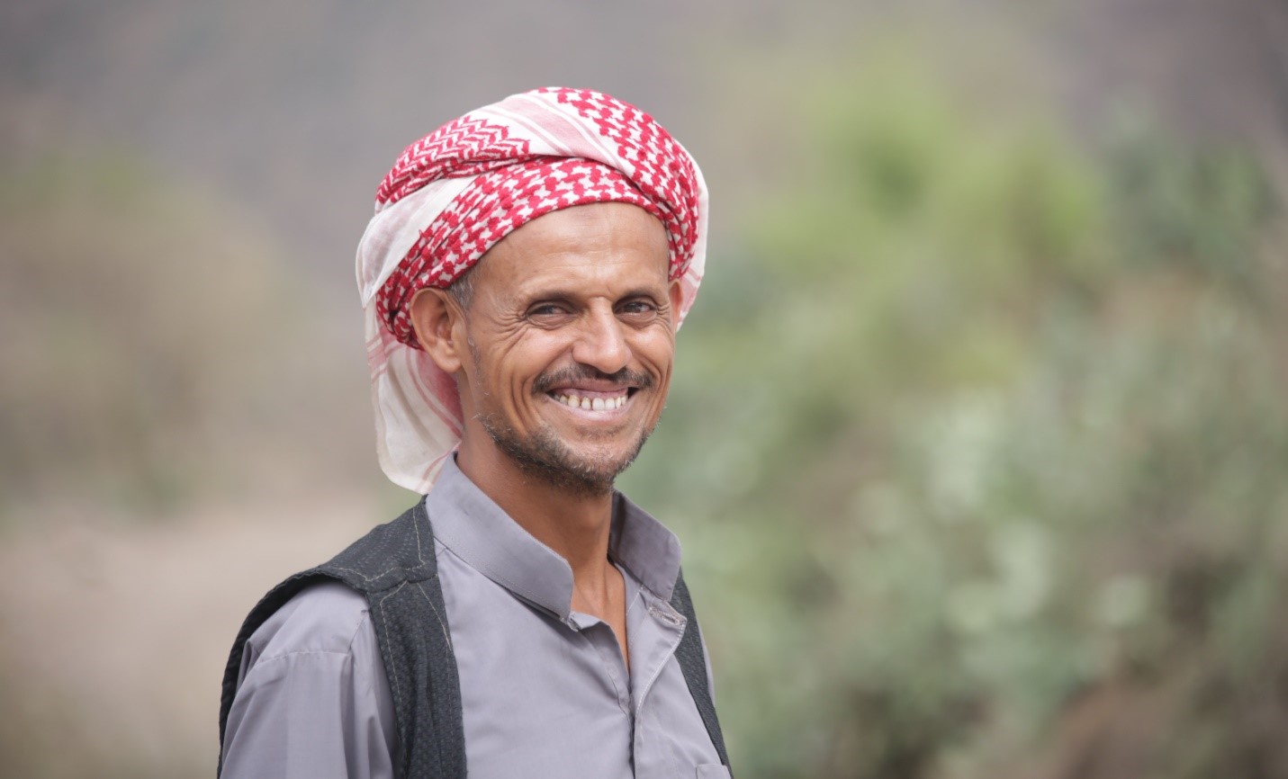 A man with a red and white headscarf smiling