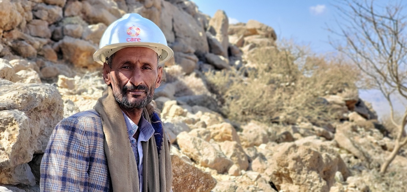 A man in a hard white helmet standing in front of rocks