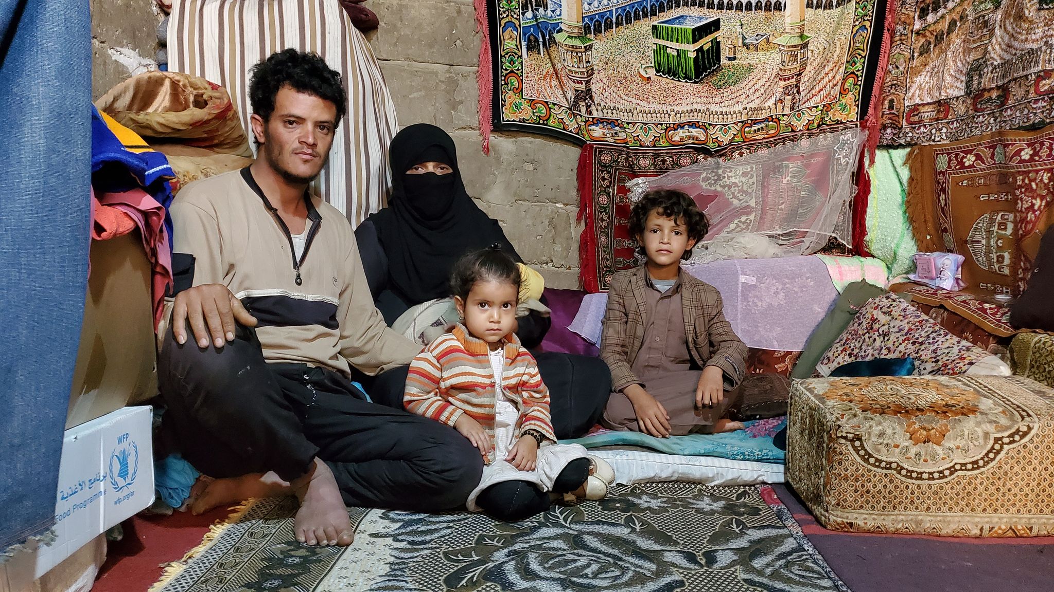 A man , woman and two kids sitting on the carpet of their House