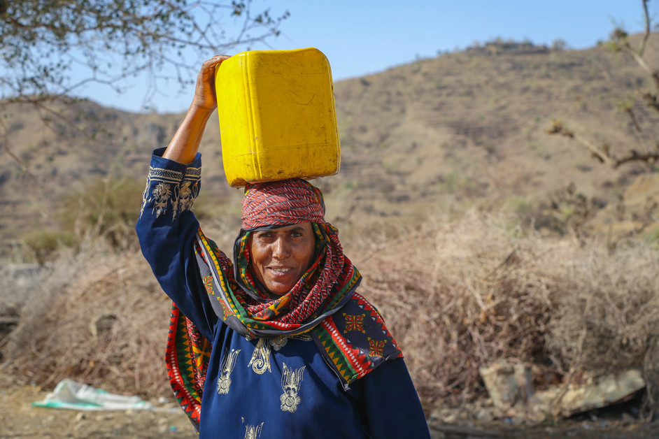 a woman carrying a yellow container on her head