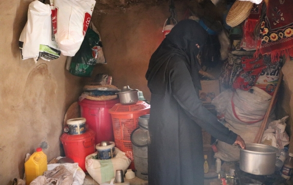 A woman in a black burka cooking in a small kitchen.