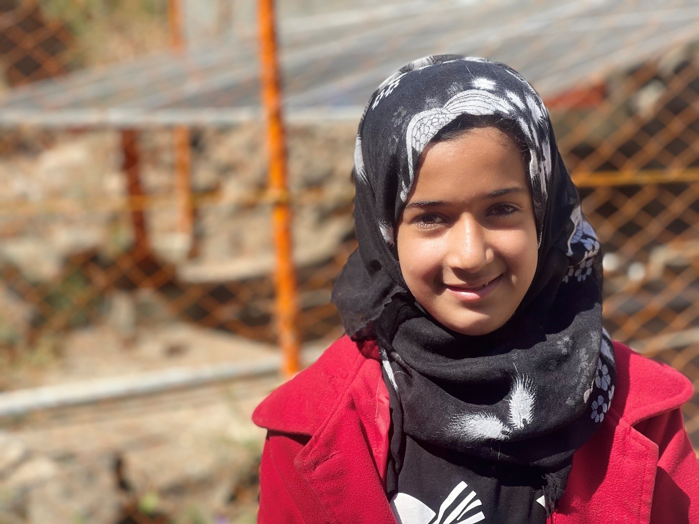 A smiling young girl in a headscarf poses for a photo.