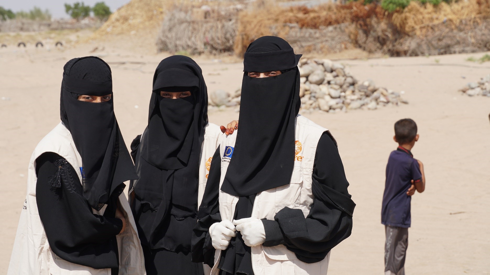Three women in black burqas standing looking at the camera