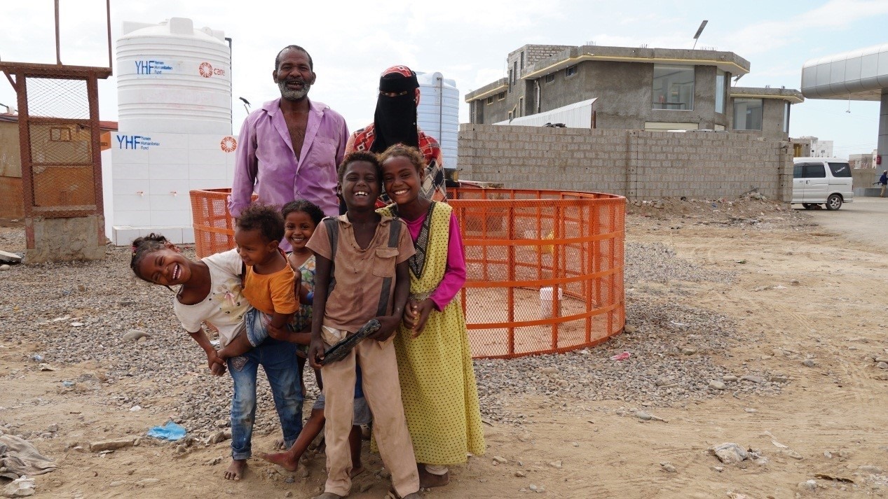 A family smiling in front of a water tank, capturing a moment of togetherness and joy.