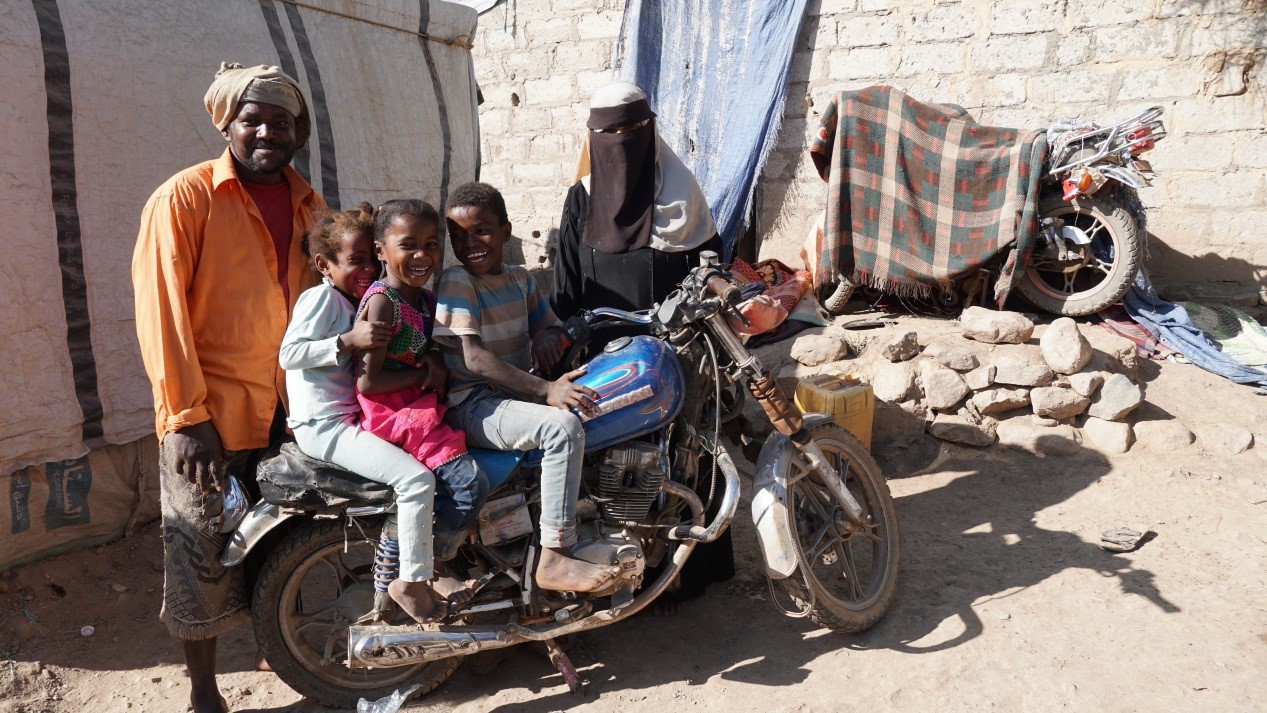 A man and two children sitting on a motorcycle in front of a tent