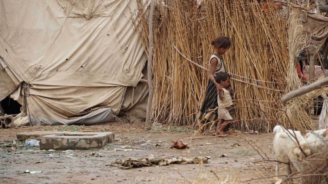Two children walking in front of a straw hut
