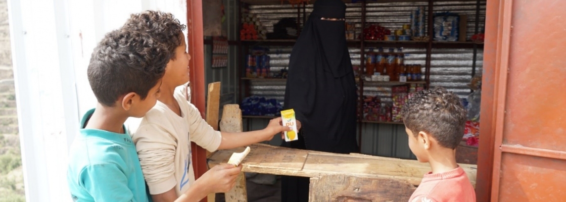 A woman with a black Burqa inside a shop with 3 young boys standing outside the shop