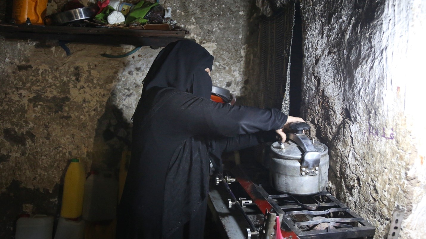 A woman wearing a black head cover cooking on a stove