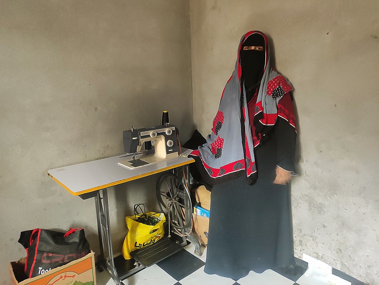 A woman in black outfit standing next to a sewing machine
