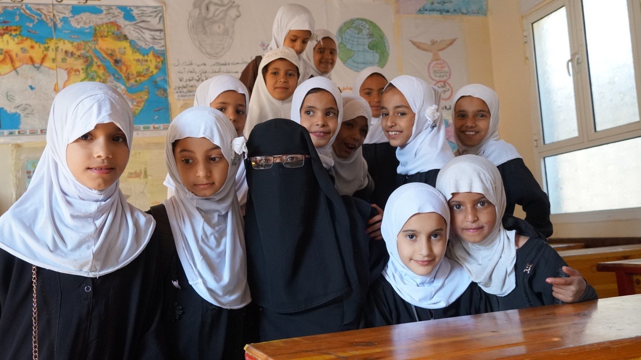 A group of young girls in white hijabs smiling and posing for a photo with a woman wearing black hijab
