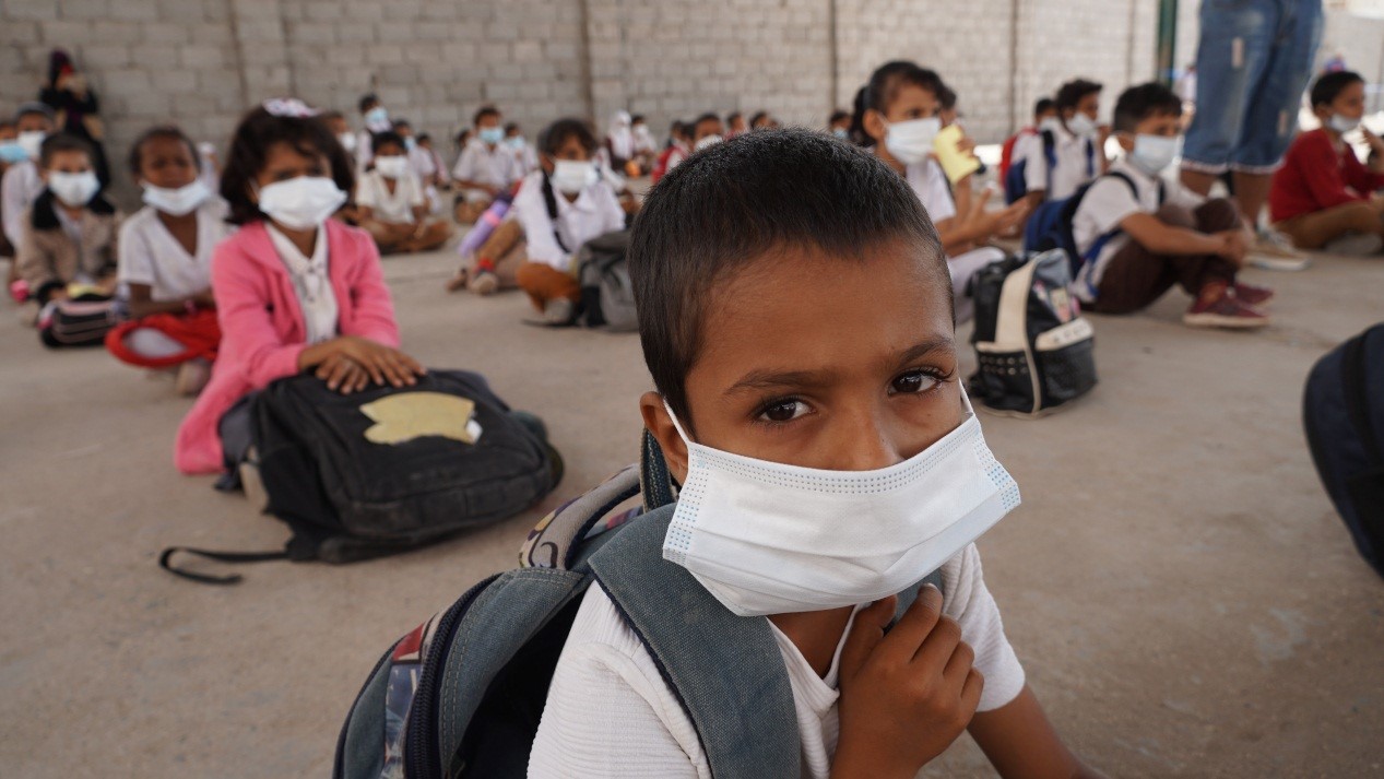 Kids wearing a face mask attentively sits in front of a classroom