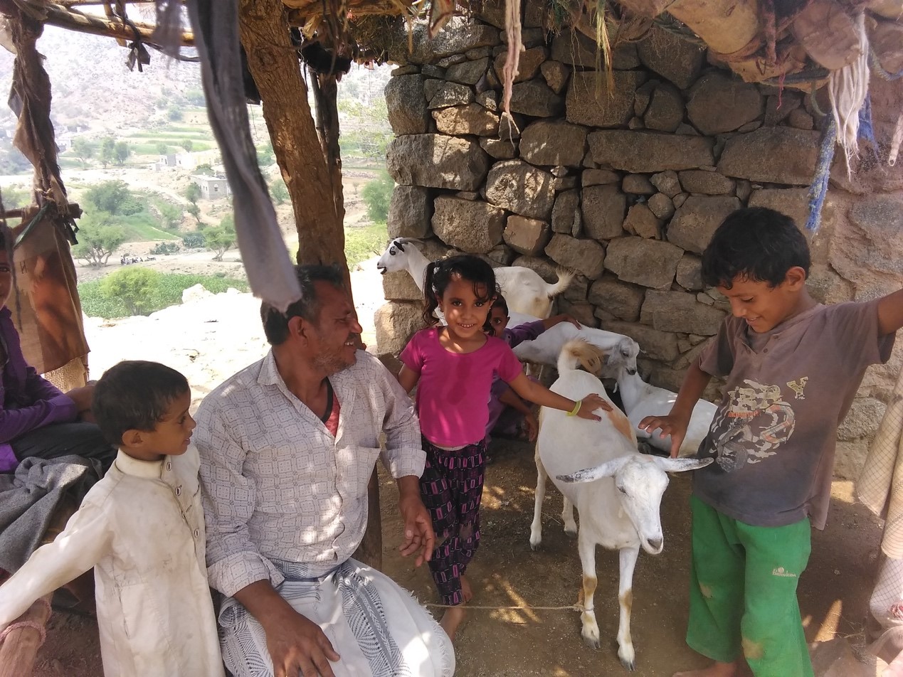 A man , kids and goats sitting under a shade