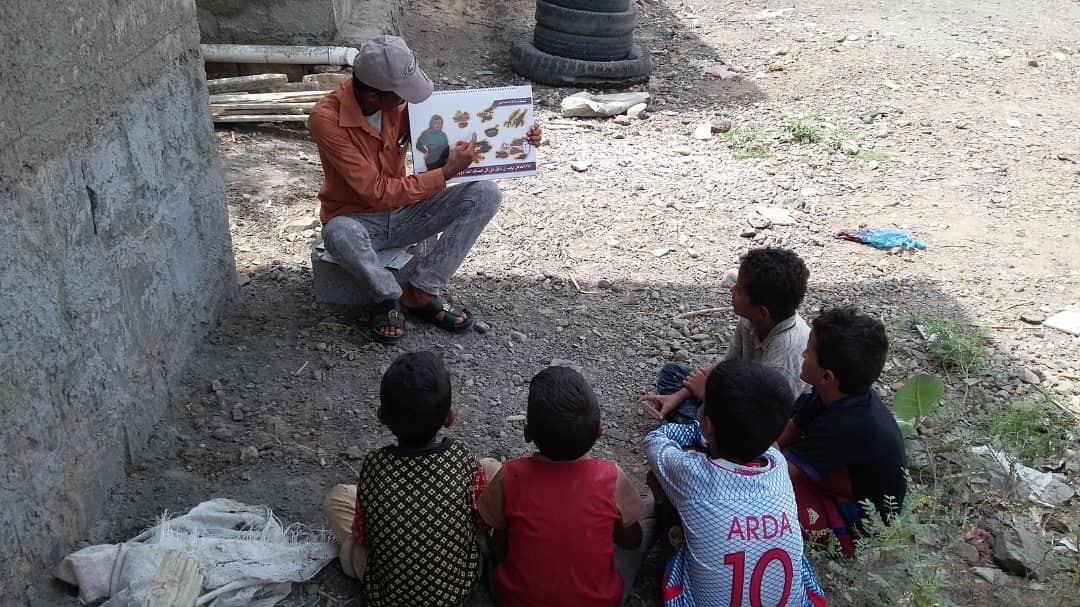 A man holding a picture with kids sitting on the ground