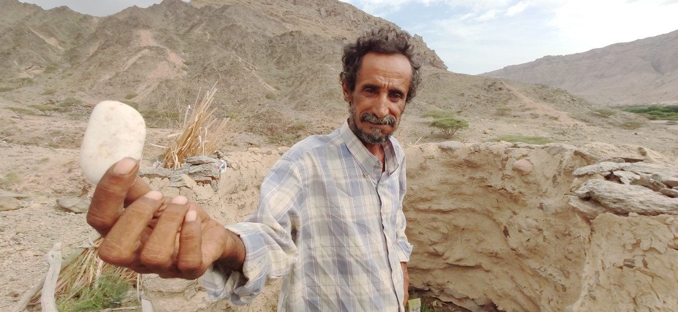 A man standing in a desert holding something white in his hand