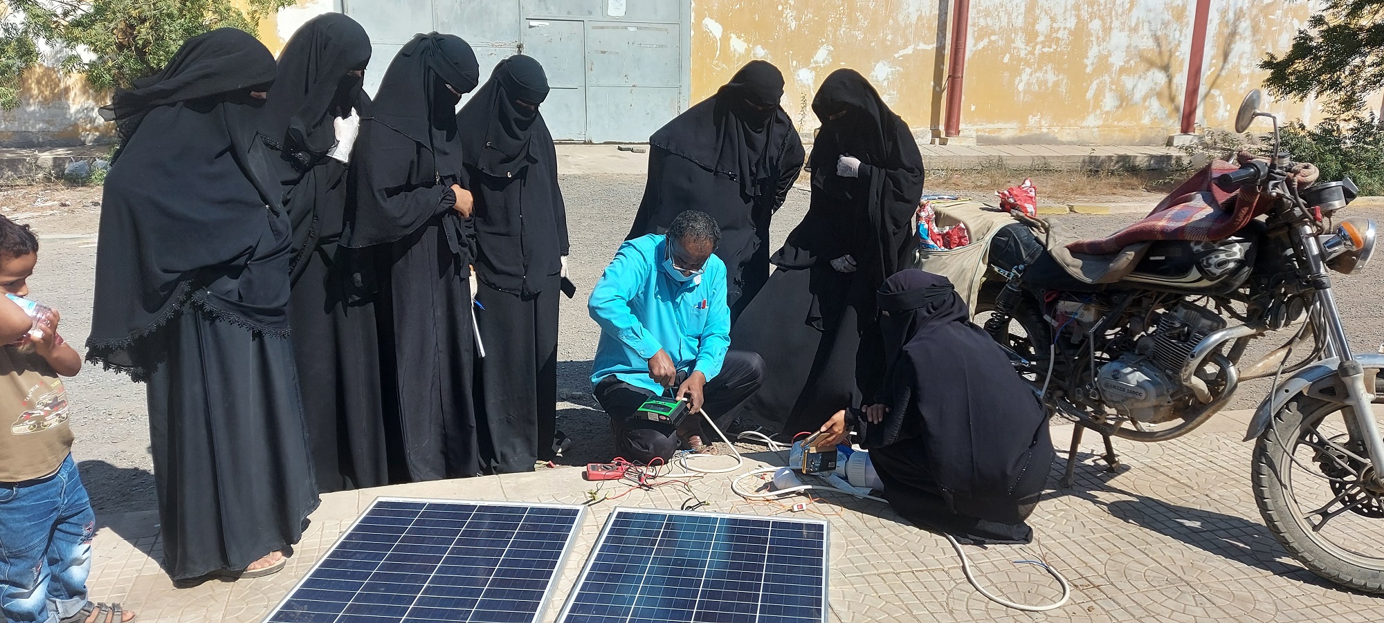 A group of women in black outfit watching a man working on a solar panel